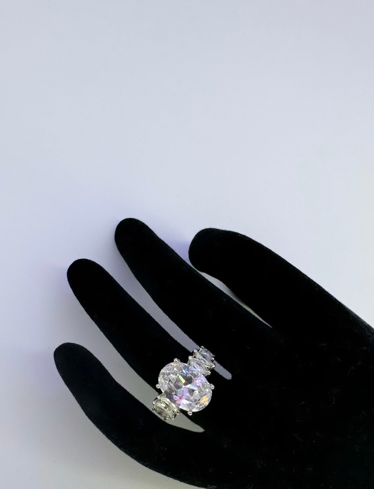 This is a large oval shaped ring as the central piece followed by mini sharply pointed white oval decorative diamonds going around the band but not entirely at the back; mainly the front of the ring. The ring is silver plated 