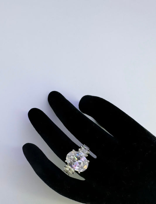 This is a large oval shaped ring as the central piece followed by mini sharply pointed white oval decorative diamonds going around the band but not entirely at the back; mainly the front of the ring. The ring is silver plated 