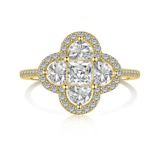 A gold plated ring with a larger central clover piece made up of different shaped white diamonds mainly mini square and semi circular diamonds with miniature white diamonds embroidered around the central piece 